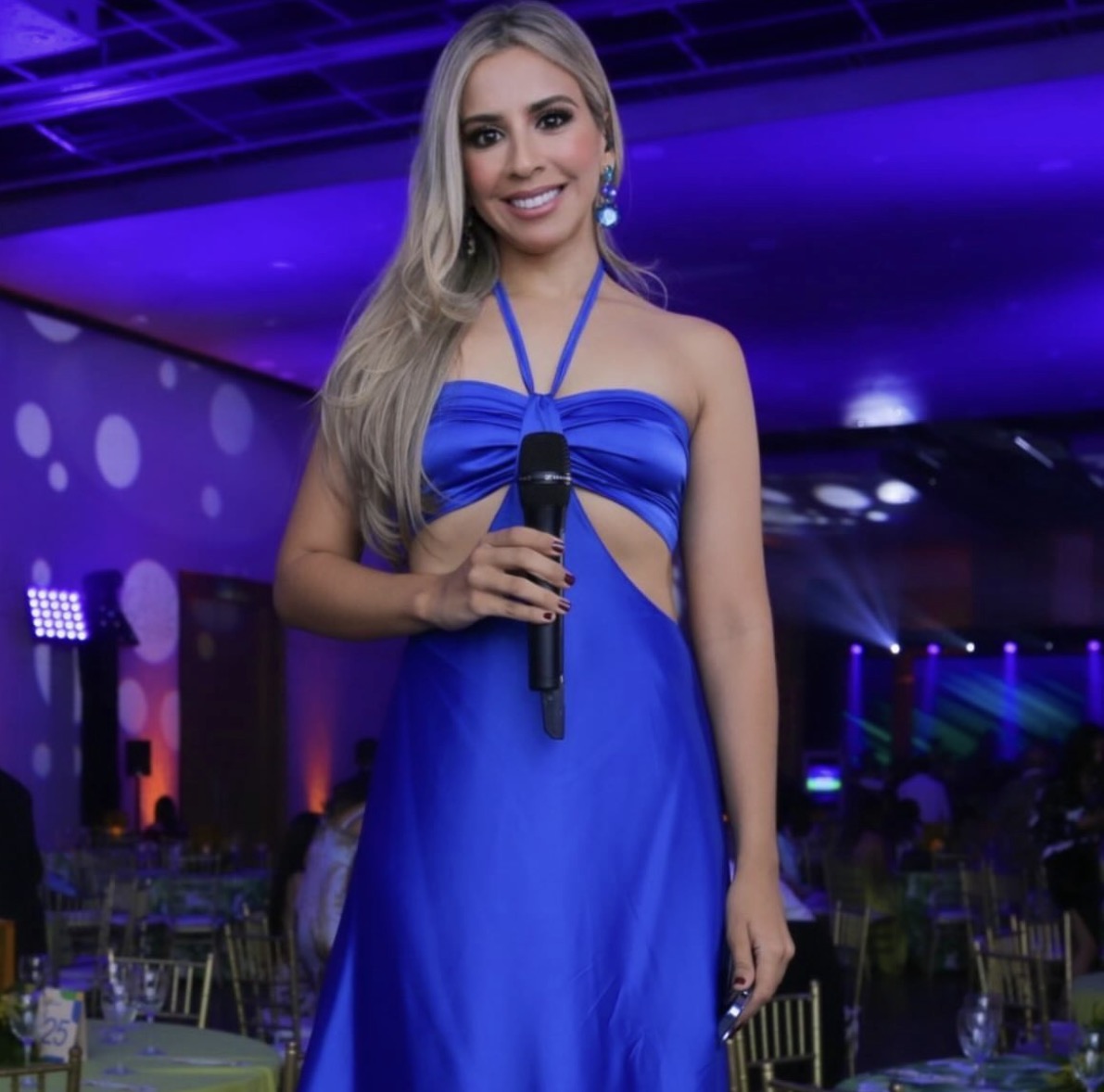 Valeria con vestido azul y micrófono en un salón de eventos